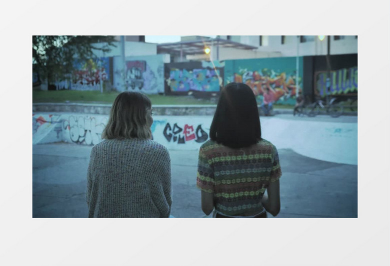 两个短发女孩坐在边上看朋友玩滑板实拍视频素材