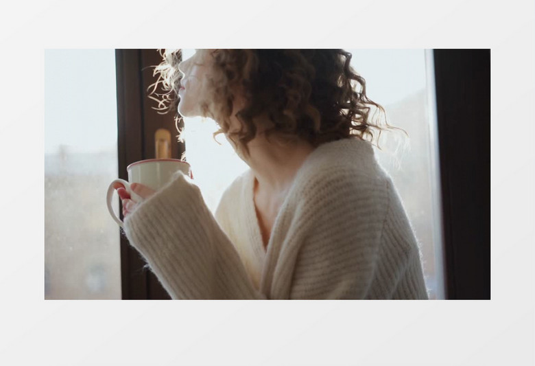 女人端着杯子站在窗前往外看实拍视频素材
