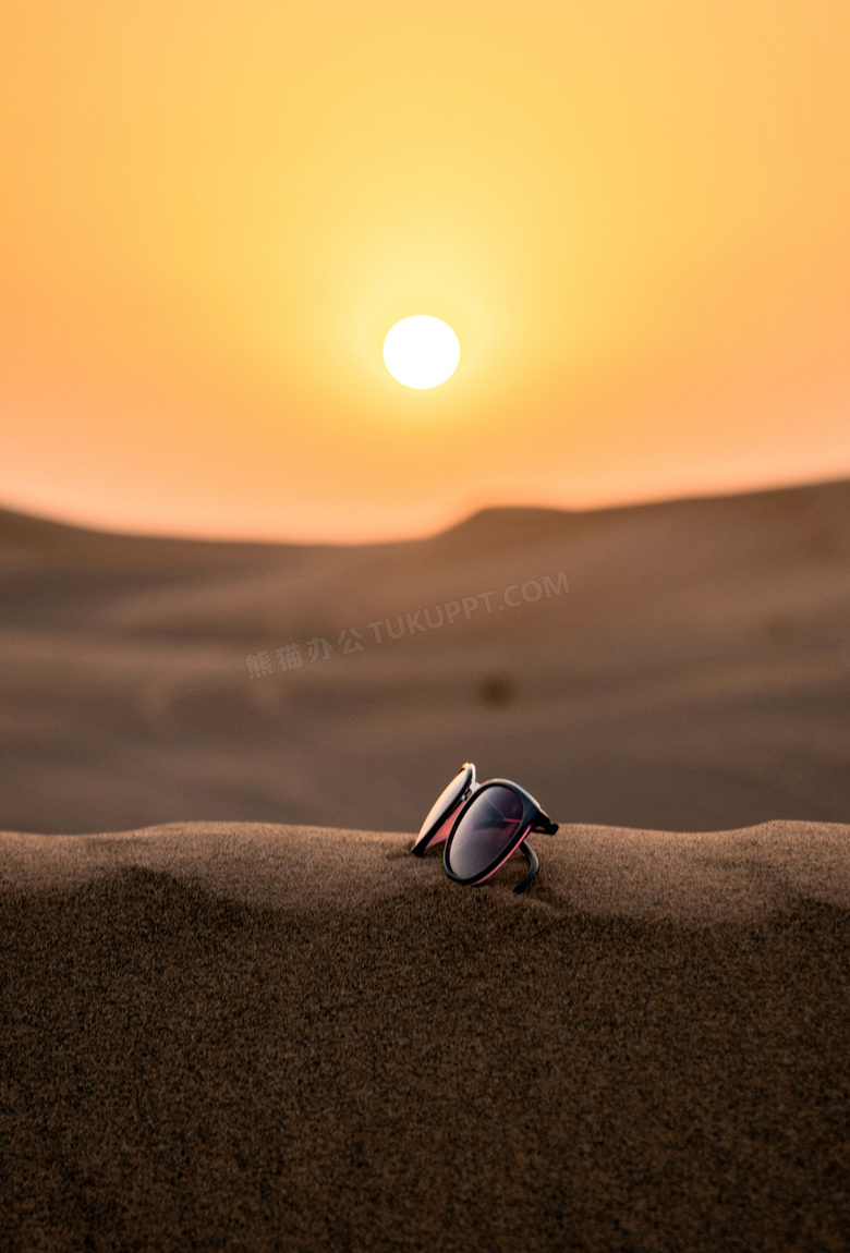 夕阳下放到沙子上的墨镜摄影图片