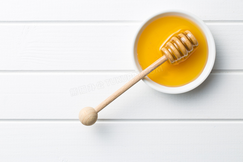 在桌上碗里的搅拌棒与蜂蜜高清图片
