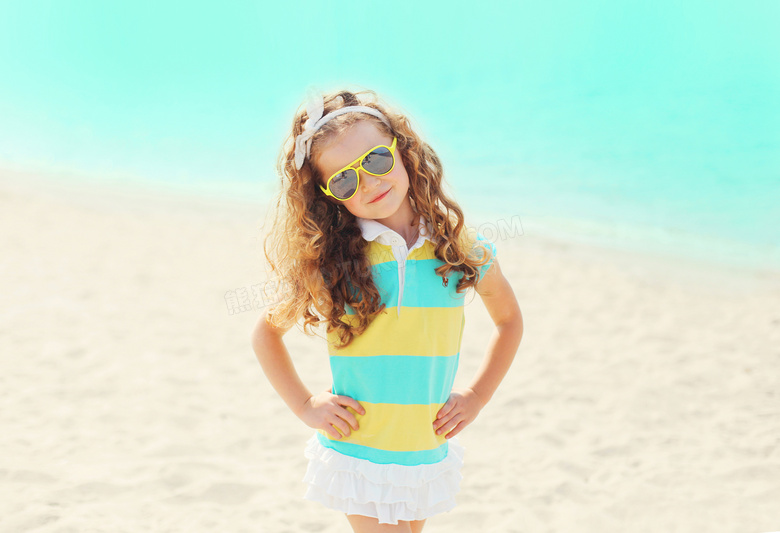 沙滩上叉着腰的卷发小女孩高清图片