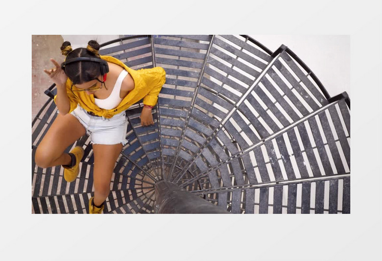 穿着黄衬衫的女孩戴着耳机坐在旋转楼梯上听音乐实拍视频素材