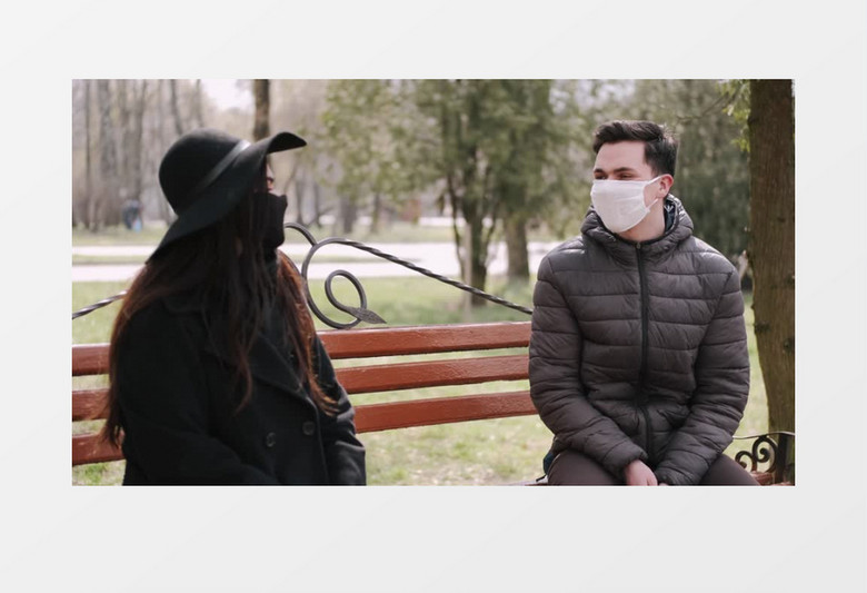 戴着口罩坐在长椅上交谈的一对情侣实拍视频素材