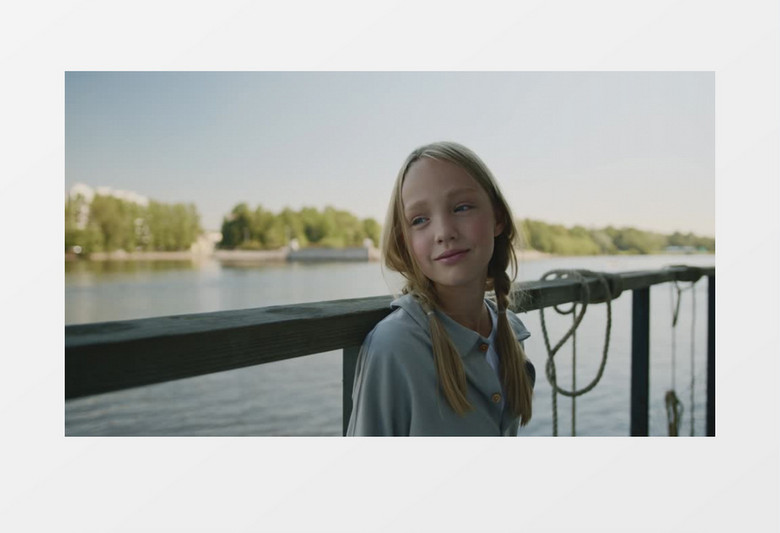 小女孩微笑着靠在湖边的栏杆上实拍视频素材